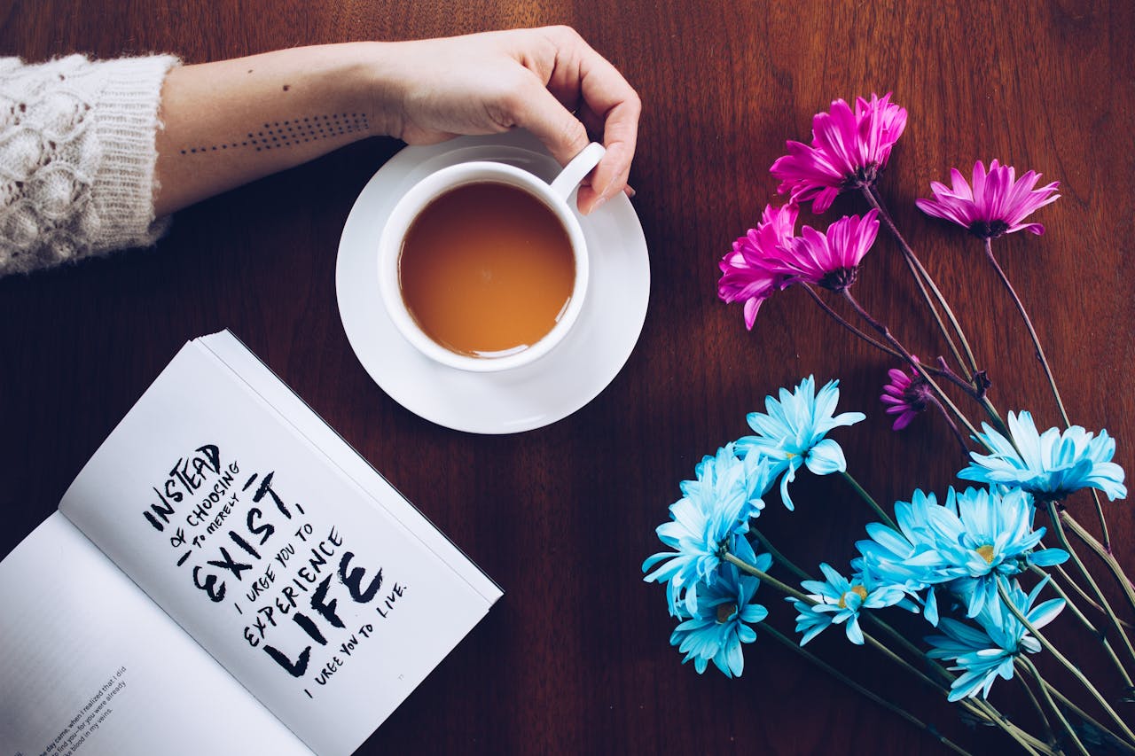 A cozy setup with tea, flowers, and an inspirational quote book on a wooden table.